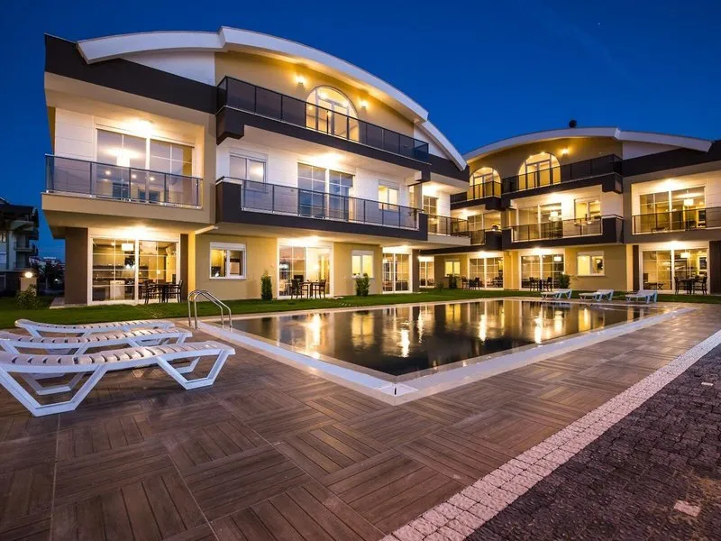 Zunanji pogled na moderno stavbo Lara Beach Homes z osvetljenim bazenom ob mraku
